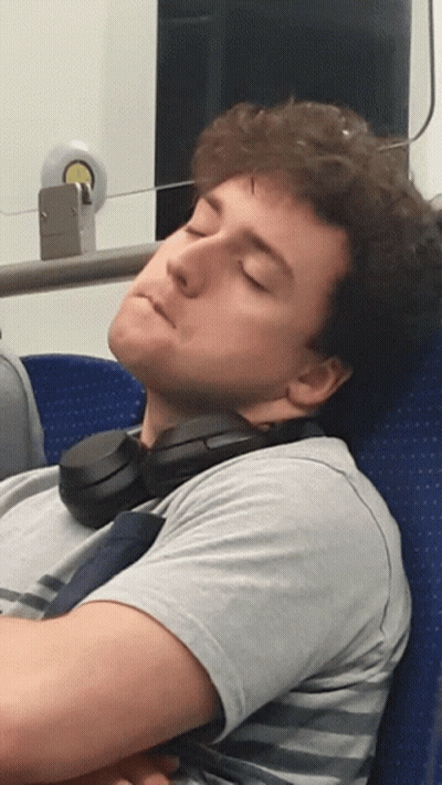 A Man With Headphones Around His Neck Is Sleeping On A Blue Seat GIF