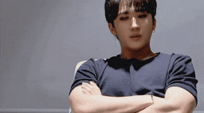 A Man With His Arms Crossed Is Wearing A Black Shirt And Earrings GIF
