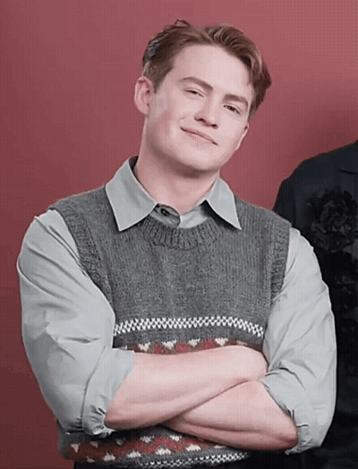A Man With His Arms Crossed Is Wearing A Grey Sweater Vest GIF