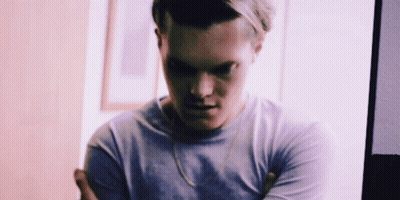 A Man With His Arms Crossed Is Wearing A Purple Shirt And A Gold Chain Around His Neck . GIF