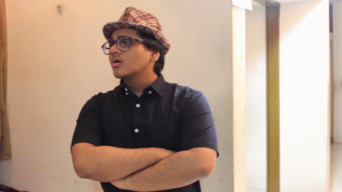 A Man With His Arms Crossed Wearing A Hat And Glasses GIF