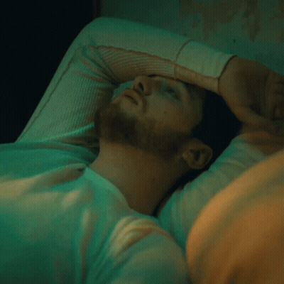 A Man With His Hand On His Forehead Is Laying In Bed GIF