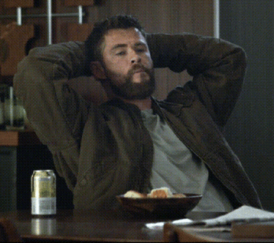 A Man With His Hands Behind His Head Sits At A Table With A Can Of Beer On It GIF