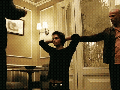 A Man With His Hands Behind His Head Stands In A Room GIF