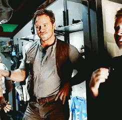 A Man With His Hands On His Hips Stands Next To Another Man In A Room GIF