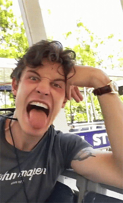 A Man With His Tongue Out Wearing A Shirt That Says John Mayer On It GIF