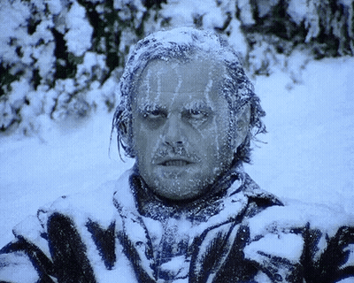 A Man With Ice On His Face Is Standing In A Snowy Field GIF