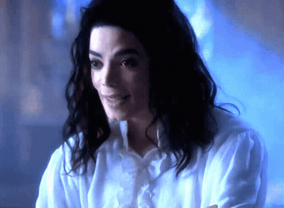 A Man With Long Black Hair And A White Shirt Is Smiling GIF