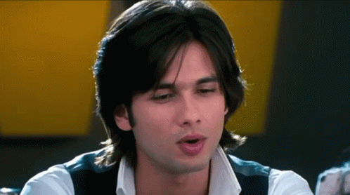 A Man With Long Black Hair Is Wearing A White Shirt And Black Vest GIF