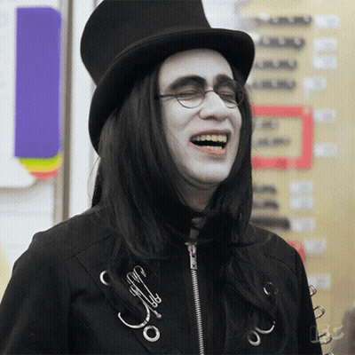 A Man With Long Black Hair Wearing A Top Hat And Glasses Laughs GIF