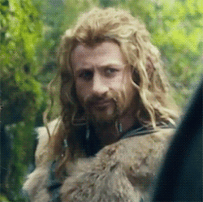 A Man With Long Blonde Hair And A Beard Is Looking At Something . GIF