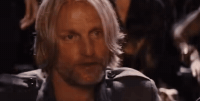 A Man With Long Blonde Hair And A Beard Is Sitting In A Dark Room With Other People . GIF