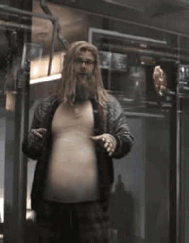 A Man With Long Blonde Hair And A Beard Is Standing In A Room . GIF