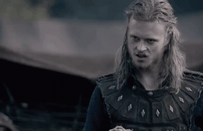 A Man With Long Blonde Hair And A Beard Is Wearing A Black Vest And A Black Shirt . GIF