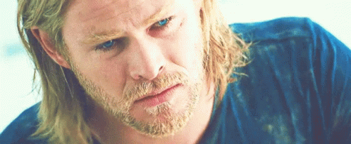 A Man With Long Blonde Hair And A Beard Is Wearing A Blue Shirt And Looking Down GIF