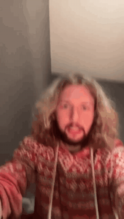 A Man With Long Blonde Hair And A Beard Is Wearing A Red Sweater And Making A Funny Face . GIF