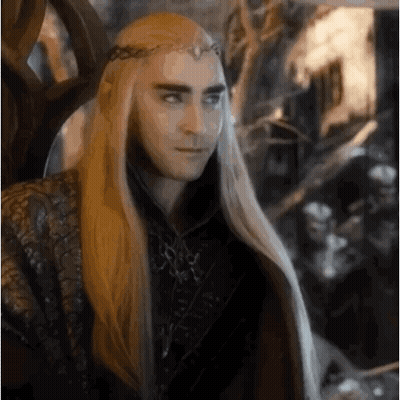 A Man With Long Blonde Hair And A Crown On His Head Is Sitting In A Throne . GIF