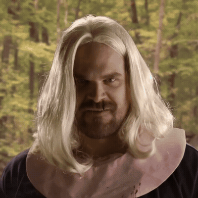 A Man With Long Blonde Hair And A Pink Bib On His Neck GIF