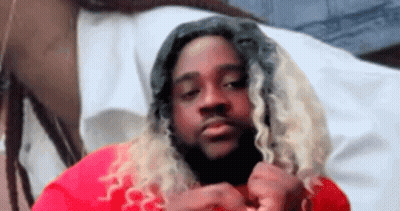 A Man With Long Blonde Hair And Dreadlocks Is Wearing A Red Shirt And Looking At The Camera . GIF