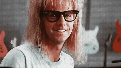 A Man With Long Blonde Hair And Glasses Is Smiling In A Classroom . GIF
