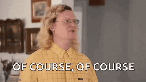 A Man With Long Blonde Hair And Glasses Is Standing In A Living Room . GIF