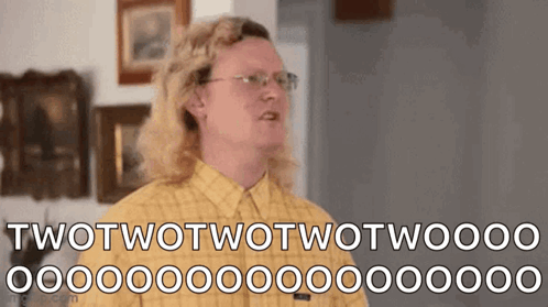 A Man With Long Blonde Hair And Glasses Is Wearing A Yellow Plaid Shirt . GIF