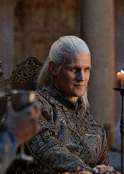 A Man With Long Blonde Hair Is Sitting In A Chair With A Candle In The Background . GIF