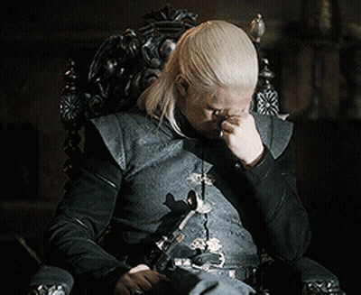 A Man With Long Blonde Hair Is Sitting In A Chair With His Hand On His Face GIF