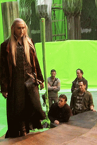 A Man With Long Blonde Hair Is Standing In Front Of A Green Background GIF