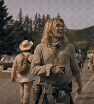 A Man With Long Blonde Hair Is Walking Down A Street With Other People GIF