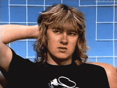 A Man With Long Blonde Hair Is Wearing A Black T-Shirt With A S On It GIF