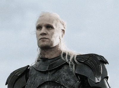 A Man With Long Blonde Hair Is Wearing Armor And Looking Up At The Sky GIF