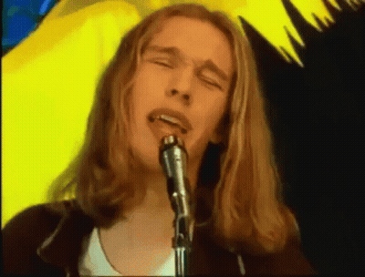 A Man With Long Blonde Hair Singing Into A Microphone GIF