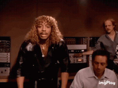 A Man With Long Curly Hair And A Mustache Is Dancing In A Room . GIF