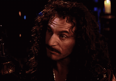 A Man With Long Curly Hair And A Mustache Looks At Something In The Dark GIF
