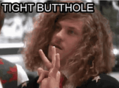 A Man With Long Curly Hair Is Making A Peace Sign And Says Tight Butthole In The Background . GIF