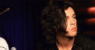 A Man With Long Curly Hair Is Sitting In Front Of A Microphone Making A Funny Face . GIF