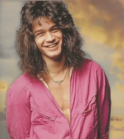 A Man With Long Curly Hair Is Smiling And Wearing A Pink Shirt GIF