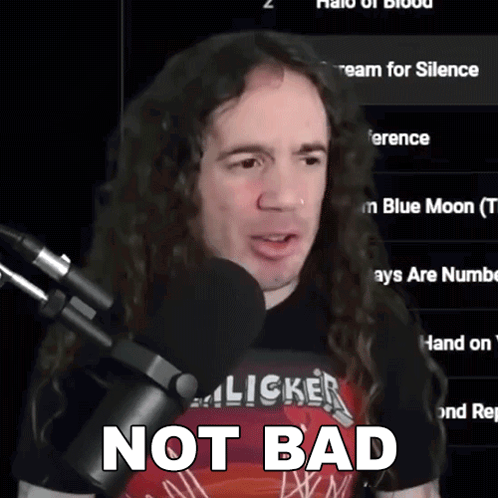 A Man With Long Curly Hair Is Standing In Front Of A Microphone With The Words Not Bad Written Below Him GIF