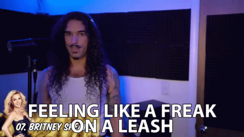 A Man With Long Curly Hair Is Standing In Front Of A Sign That Says " Feeling Like A Freak " GIF