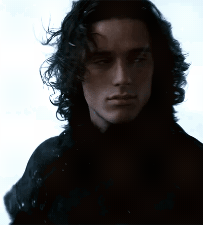 A Man With Long Curly Hair Is Wearing A Black Shirt GIF
