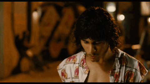A Man With Long Curly Hair Is Wearing A Shirt That Says ' A ' On It GIF