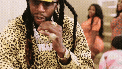 A Man With Long Dreadlocks Is Wearing A Leopard Print Jacket And A Hat . GIF