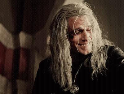 A Man With Long Grey Hair Is Smiling And Wearing A Pendant GIF