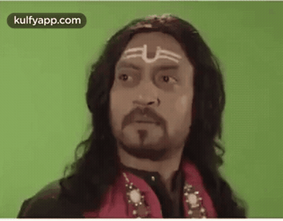 A Man With Long Hair , A Beard And A Tattoo On His Forehead Is Wearing A Red Jacket . GIF