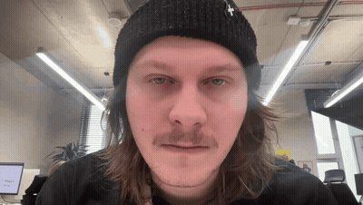 A Man With Long Hair And A Beanie With A Cross On It GIF
