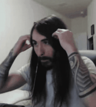 A Man With Long Hair And A Beard Adjusts His Headphones GIF