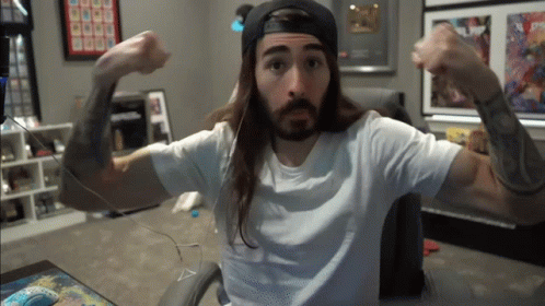 A Man With Long Hair And A Beard Is Flexing His Arms GIF