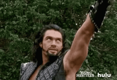 A Man With Long Hair And A Beard Is Holding A Sword In The Air . GIF