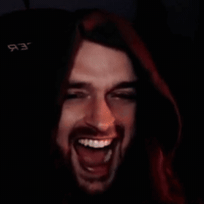 A Man With Long Hair And A Beard Is Laughing In A Dark Room With A Black Background GIF